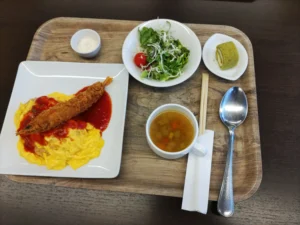 セキュリティキャンプの昼食 中央に野菜スープ、その左隣にエビフライの乗ったオムライス、右上にサラダと抹茶ロールケーキ
